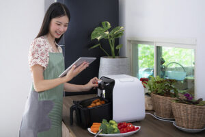 Asian female is cooking with her Air Fryer making a fried chicken for dinner by using very little oil. 