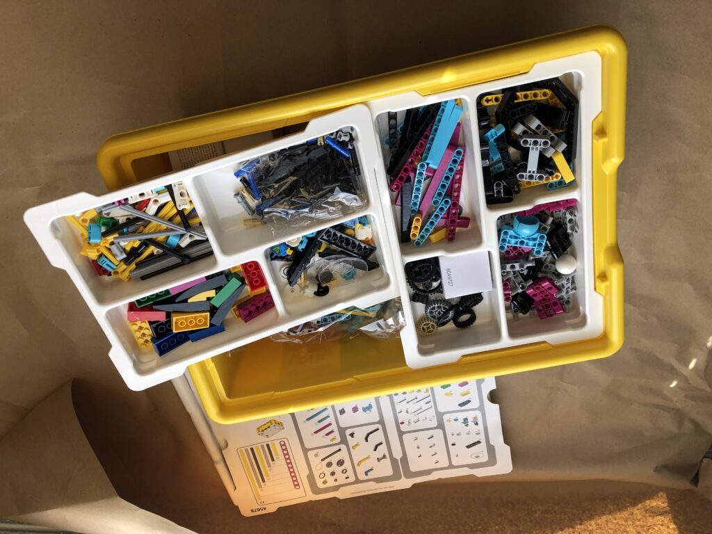 A box containing LEGO bricks of various sizes and colors sits on top of a page containing instructions on assembling items.