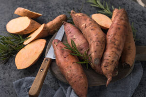 Sweet potato on wooden board background, close up. Raw sweet potatoes or batatas with herbs, Sweet potato