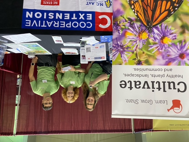 Information booth, three individuals behind a table with papers on top.